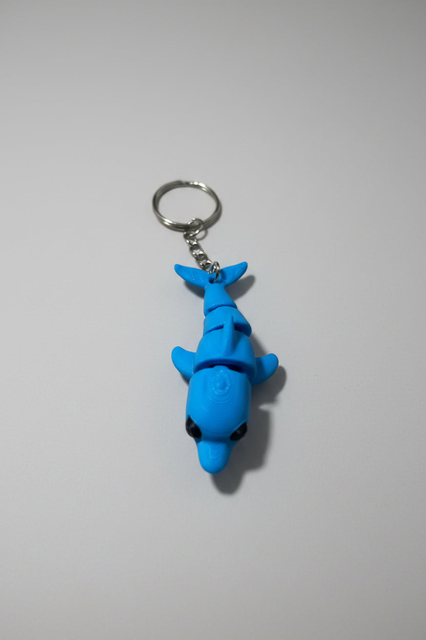 Porta-chaves golfinho articulado impresso em 3D em azul, vista lateral sobre mesa de madeira